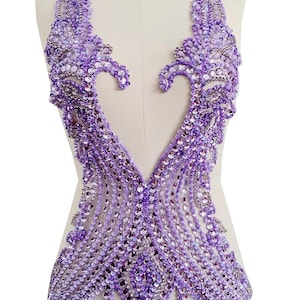 Puede incluir: Un corpiño de color lavanda con cuentas y un diseño de cuello en V profundo. El corpiño está profusamente adornado con pedrería y lentejuelas brillantes, creando un efecto brillante. El diseño presenta patrones intrincados y una espalda abierta.