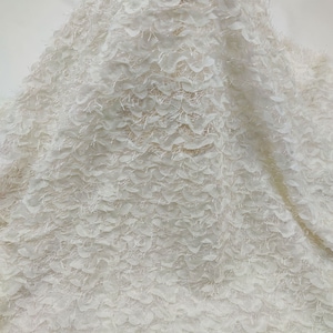 Pode incluir: Tecido branco com um padrão texturizado, felpudo e ligeiramente ondulado. O tecido tem uma aparência delicada, quase como penas.