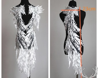 Peut inclure: Design textile blanc et plumeux, présenté sur un mannequin noir. Le design mesure environ 100 cm de long et 23 cm de large. Le textile a un aspect délicat et superposé, avec un motif central ouvert. L'esthétique générale est élégante et éthérée.
