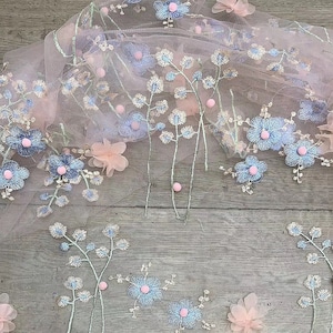 May include: Pink and blue floral embroidered tulle fabric with small pink beads. The fabric has a delicate and feminine design.
