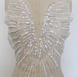 May include: White beaded and sequined lace applique in the shape of wings. The applique is perfect for adding a touch of elegance to any garment.