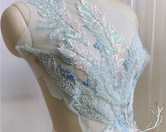 Peut inclure: Une applique de sequins et de perles irisés bleu clair avec un motif floral sur un tissu de maille transparent.