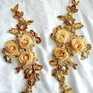 May include: Two gold lace appliques with beige fabric flowers and iridescent rhinestones. The appliques are perfect for adding a touch of elegance to clothing, accessories, or home decor.