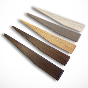 May include: Six wooden spatulas in varying shades of brown, from light beige to dark walnut. Each spatula has a long, tapered handle and a wide, rectangular head. The wood grain is visible on each spatula, adding to their natural aesthetic.