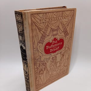 Op de afbeelding: Een vintage boek met een bruinachtige kaft met de titel "Die Butaniere vom Broof" in het rood en illustraties van mensen. De rug heeft de naam van de auteur, W. Petersen, en de titel. De kaft van het boek heeft een decoratief ontwerp.