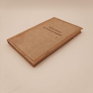 Op de afbeelding: Een vintage boek met een bruin linnen omslag. De titel en auteur van het boek zijn gedrukt in zwarte inkt. Het boek is rechthoekig en heeft een bruine rand.