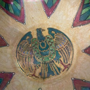 May include: A vintage ceramic bowl featuring a gold and green eagle design in the centre. The bowl has a cream background with red, green, and blue geometric patterns surrounding the eagle.