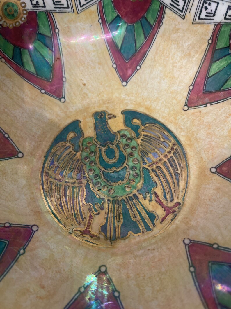 May include: A vintage ceramic bowl featuring a gold and green eagle design in the centre. The bowl has a cream background with red, green, and blue geometric patterns surrounding the eagle.