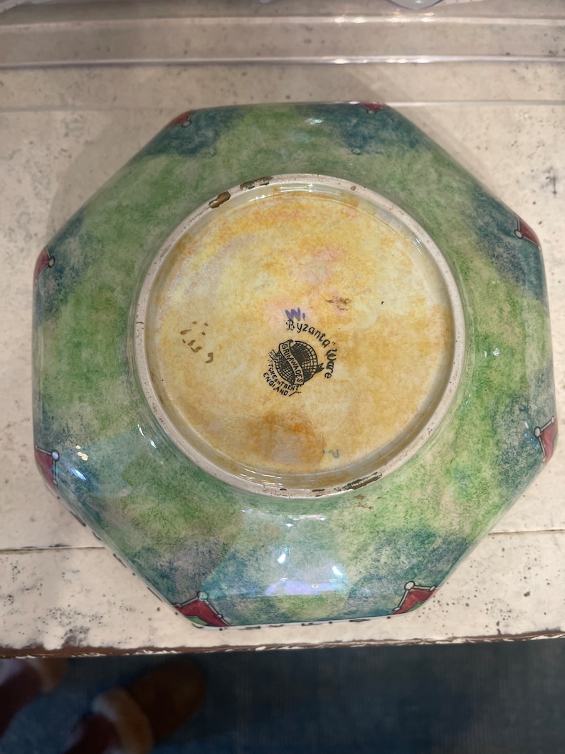 May include: Octagonal green and blue ceramic bowl with red accents. The bottom of the bowl has a white label with the text "Byzantia Ware" and "England".