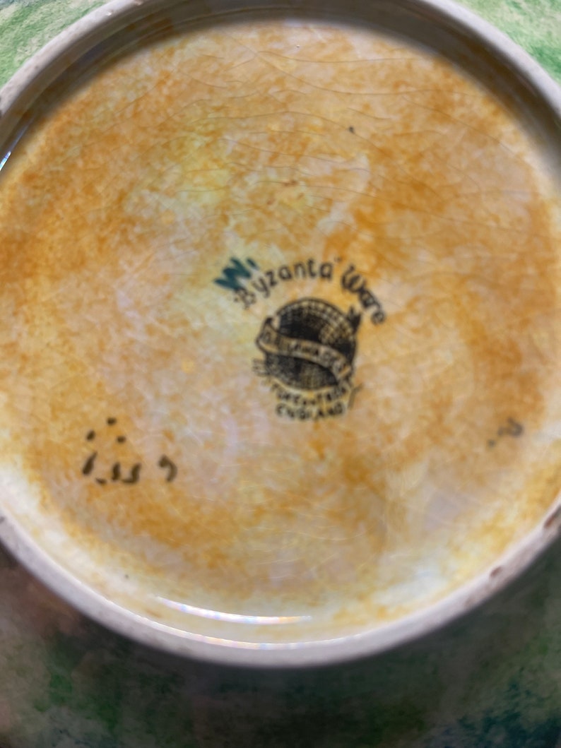 May include: Close-up of the underside of a ceramic plate with a brown glaze. The plate features a black and white logo that reads "W. Bizanta Ware" and "Pottery Made in England". The number "113" is written in black on the base of the plate.