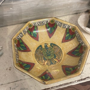May include: Octagonal ceramic bowl with a yellow glaze and a colourful design. The design features a stylised bird with green, red, and blue accents. The bowl has a gold rim.