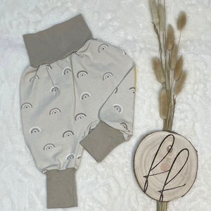 Peut inclure: Pantalon bébé beige avec un imprimé arc-en-ciel. Le pantalon a une large ceinture élastique et des jambes retroussées.