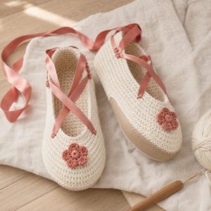 May include: A pair of off-white crochet slippers featuring a rounded toe, a single dusty rose crocheted flower accent on the front, and long dusty rose satin ribbon laces that crisscross over the top of the foot and tie around the ankle.