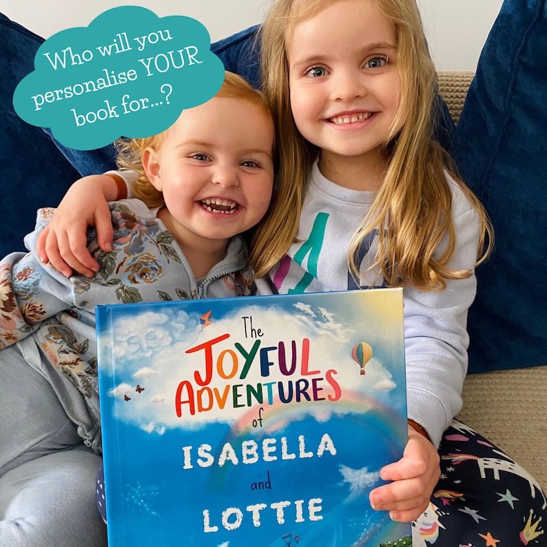 May include: Two young girls smiling and holding a personalized book titled "The Joyful Adventures of Isabella and Lottie." The book cover features a blue sky, rainbow, and hot air balloon. Text above the girls says, "Who will you personalize YOUR book for...?"