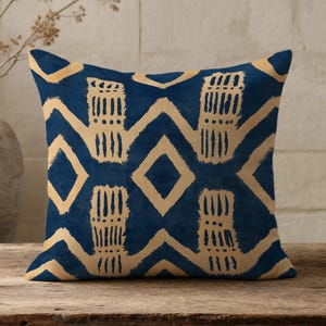 May include: A square throw pillow featuring a deep navy blue background with a repeating pattern of light tan, hand-painted style zig-zag lines and diamond shapes. The design creates a bold, high-contrast geometric motif across the fabric surface.