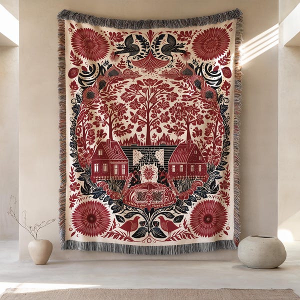 May include: A rectangular woven throw blanket featuring a cream background with a symmetrical folk-art design in deep red and black. The pattern depicts two houses, trees, and birds, finished with a fringed edge along the top and bottom borders.
