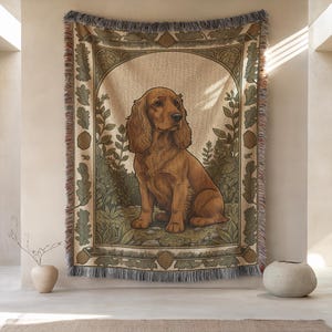 Può includere: Arazzo tessuto raffigurante un cane Cocker Spaniel dorato in un ambiente naturalistico. Il cane è il punto focale, circondato da un fogliame stilizzato nei toni del verde e del marrone. L'arazzo ha un bordo con frange e uno sfondo neutro.