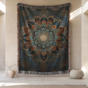 May include: A rectangular woven throw blanket featuring a large, intricate mandala design in shades of deep teal, navy blue, and burnt orange. The blanket has a fringed edge along the top and bottom, with detailed symmetrical floral patterns.