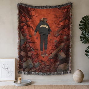 May include: Woven throw blanket featuring an illustration of a person floating in a surreal, fiery landscape. The person wears a black jacket with a white stripe, black pants, and headphones. The background is a mix of red, brown, and gray tones.