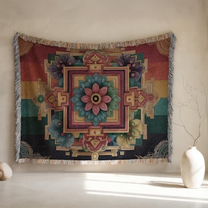 May include: A tapestry with a geometric floral design in shades of red, teal, pink, and gold. The tapestry has a fringed edge and is hanging on a wall. The central design is a flower within a square, surrounded by other geometric shapes.