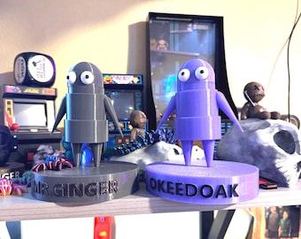 May include: Two 3D printed figurines, one gray and one purple, stand on bases with the names "Mr. Ginger" and "OkeeDoak" printed on them.
