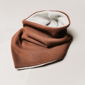 Op de afbeelding: Een bruine wafel gebreide nekwarmer met een witte fleece voering. De nekwarmer is dubbelgevouwen en de witte voering is zichtbaar.