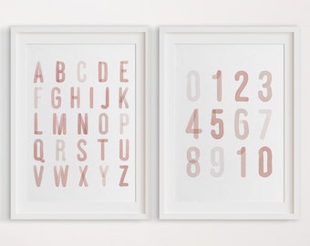 May include: Two framed prints with a white background. The left print features the alphabet in pink and white watercolor letters. The right print features the numbers 0-10 in pink and white watercolor numbers. The prints are titled "Bedtime Bear Prints // On Etsy".