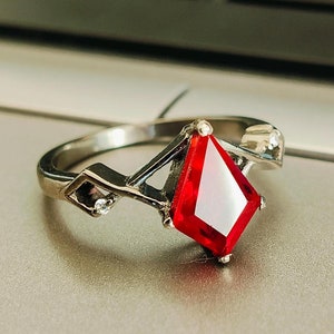 May include: A silver ring featuring a large, red, faceted gemstone at its centre. The ring has a delicate, geometric design with smaller clear gemstones on the band.