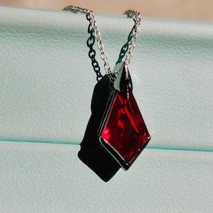 Peut inclure: Un collier en chaîne argent avec un pendentif en pierre rouge. Le pendentif est de forme géométrique facetté.