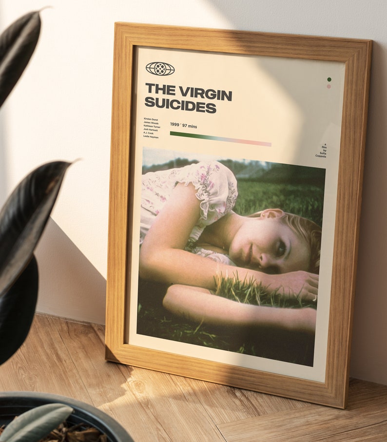 May include: A framed poster with a minimalist design featuring a photo of a young woman lying in a field of grass. The poster is titled "The Virgin Suicides" and includes the year 1999 and the runtime of 97 minutes.