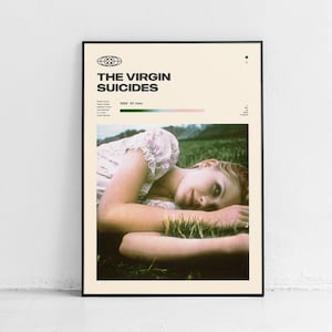 May include: A movie poster for the film "The Virgin Suicides" featuring a woman lying in a field of grass. The poster is in a black frame and has a cream background with black text. The text on the poster reads "The Virgin Suicides" and "1999 - 97 mins".