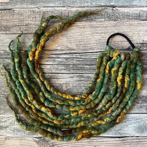 Könnte beinhalten: Grüne und gelbe Wolldreads mit einem braunen Gummiband.