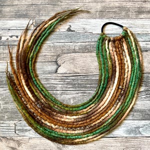 Könnte beinhalten: Handgefertigte Dreadlocks in Braun-, Grün- und Beigetönen, kreisförmig angeordnet. Die Dreadlocks sind an einem schwarzen Gummiband befestigt. Einige Dreadlocks haben dekorative Nähte und kleine Metallakzente.