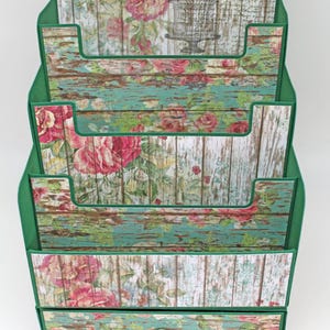 Könnte beinhalten: Ein dreistöckiger grüner und weißer Holzorganizer mit einer Schublade. Der Organizer hat ein Blumenmuster mit Rosen und einem Vogelkäfigdesign. Die Schublade hat einen grünen Knopf.