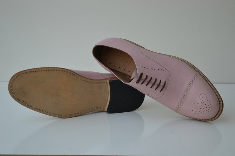 May include: A pair of pink leather oxford shoes with a brogue design and a brown leather sole.