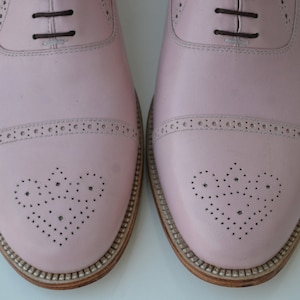 May include: A pair of pink leather oxford shoes with a brogue design and lace-up closure.