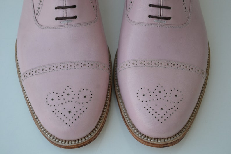 May include: A pair of pink leather oxford shoes with a brogue design and lace-up closure.