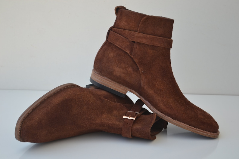 Pode incluir: Botas de tornozelo de camur&ccedil;a marrom com uma fivela e bico fino.