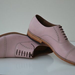 May include: A pair of pink leather lace-up shoes with brogue detailing. The shoes have a rounded toe and a low heel.