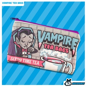 May include: A grey zipped pouch with a cartoon vampire drinking tea. The pouch has the text "Vampire Tea Bags" and "Sleepy Time Tea" printed on it.