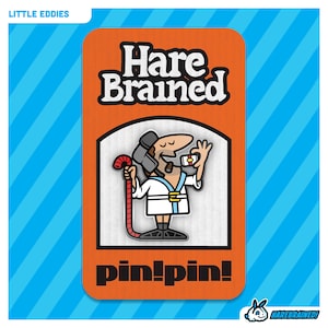 May include: Orange and white enamel pin featuring a cartoon character wearing a white robe and a helmet, holding a red pipe and a small white box. The text "Hare Brained" is at the top of the pin and "pin!pin!" is at the bottom.