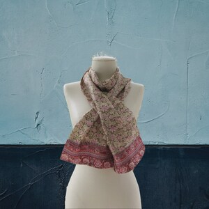 May include: A floral patterned scarf with a pink and green design and a red border. The scarf is displayed on a white mannequin.