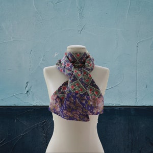 May include: A patterned scarf with a floral design on one side and a geometric design on the other side. The scarf is tied around a white mannequin's neck.