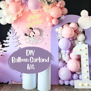 May include: DIY balloon garland kit with pink, white, and purple balloons, a large white number one with lights, and a backdrop with a Minnie Mouse design and the words "Happy Birthday".