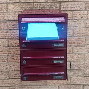 May include: A red metal mailbox with five compartments, one labeled "LANDLORD". A blue piece of paper is sticking out of the top compartment.