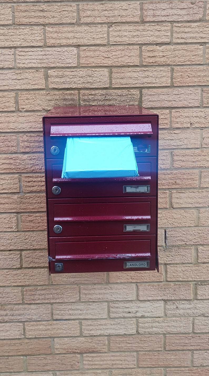 May include: A red metal mailbox with five compartments, one labeled "LANDLORD". A blue piece of paper is sticking out of the top compartment.