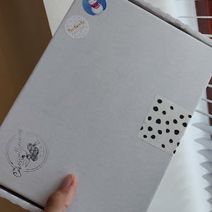 May include: A white cardboard box with a black and white polka dot sticker, a snowman sticker, and a sticker that says "Handmade with Love". The box also has a black and white logo that says "Cakespellings" with a cupcake graphic.