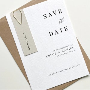 Puede incluir: Una tarjeta blanca de guardar la fecha con texto negro que dice "Save the Date" para la boda de Chloe & Daniel, Lago de Garda, Italia. La fecha 09.03.2023 est&aacute; impresa en una tarjeta beige separada.