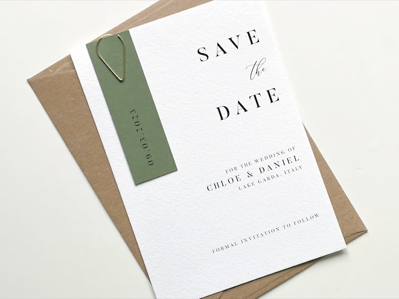 Puede incluir: Tarjeta de guardar la fecha con una etiqueta verde adjunta. La tarjeta dice "Save the Date" en texto negro con un "the" escrito a mano. El texto debajo dice "For the wedding of Chloe & Daniel, Lake Garda, Italy" y "Formal invitation to follow". La etiqueta dice "09.03.2023" en texto negro.