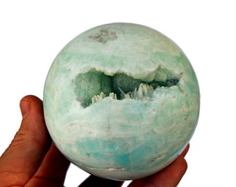 May include: A green and white agate sphere with a large, open cavity revealing a crystal formation inside.